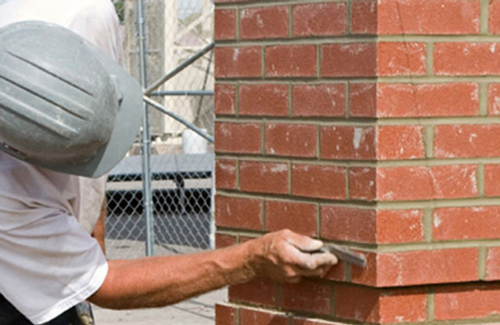 A man diligently constructs a brick wall, carefully placing each brick with precision and focus on his work.