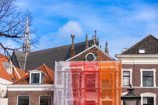 A vibrant red and orange mesh drapes over a modern building, creating a striking visual contrast against the structure.